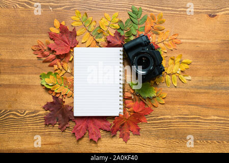 Blank sheet of copybook surrounded by colorful autumn leaves with photocamera Stock Photo