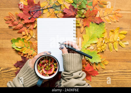 Overview of student hands holding hot herbal tea and pen over open copybook Stock Photo