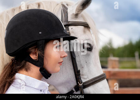 Profile of young active woman in equestrian helmet and white purebred horse