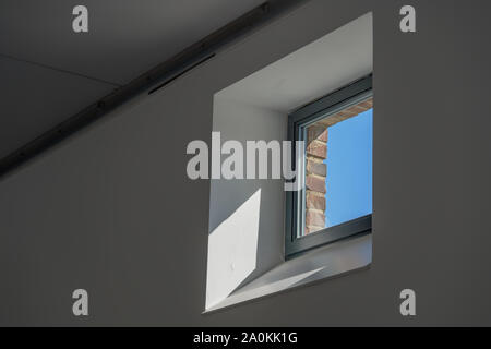 Interior view of square single window with thick new inner white wall, clear transparent glass, black frame and outer old brick wall. Stock Photo