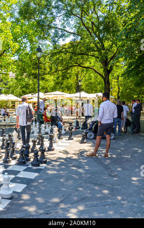 Geneva, Switzerland - July 19, 2019: People playing outdoor chess game with giant chess figures in the Parc des Bastions. Big chess boards are located at the entrance to the park in the city center. Stock Photo