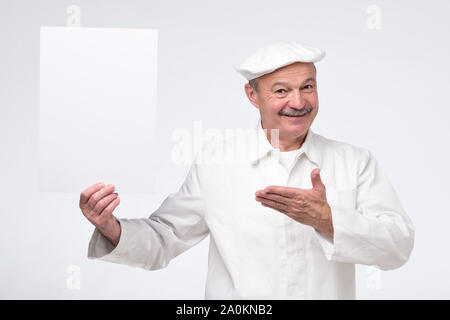 Joyful attractive hispanic mature chef cook holding copy space on his palm, looking at camera smiling, presenting new menu Stock Photo