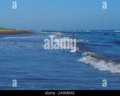 Gentle sea waves approaching the sandy beach at Mablethorpe, Lincolnshire, England, with a clear blue sky Stock Photo