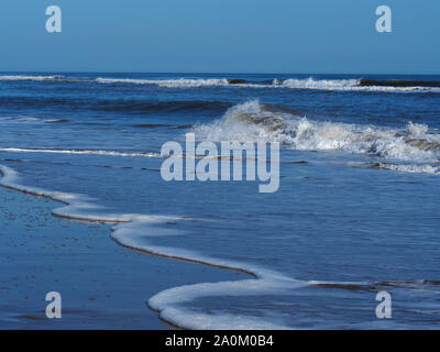 Breaking waves with white surf and a clear blue sky at Mablethorpe, Lincolnshire, England Stock Photo