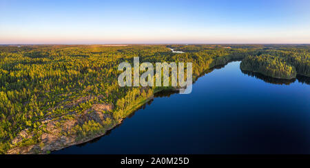 Endless woodland aerial panoramic view. Deep wild forest and clear blue lake at sunset Stock Photo