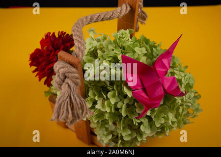 origami butterfly crafted art on a green bush in a basket on a colored background beautiful bouquet studio close shot Stock Photo