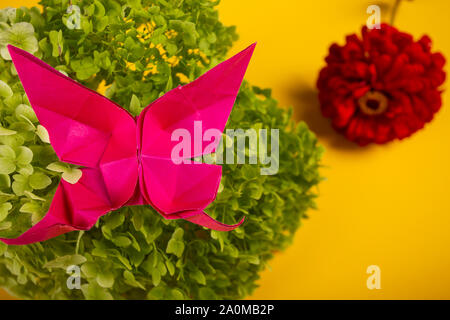 origami handmade crafted butterfly on a green bush in a basket on a colored background beautiful bouquet studio close shot Stock Photo