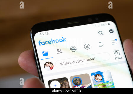 A man holding a smartphone showing the Facebook app and logo Stock Photo