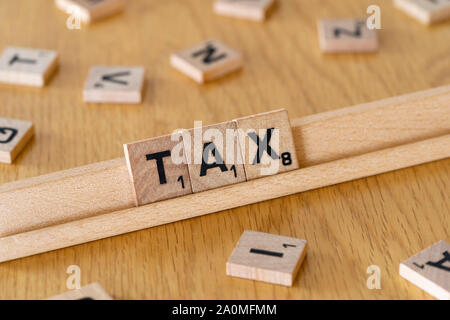 Wooden scrabble letters on a rack spelling out the word Tax Stock Photo