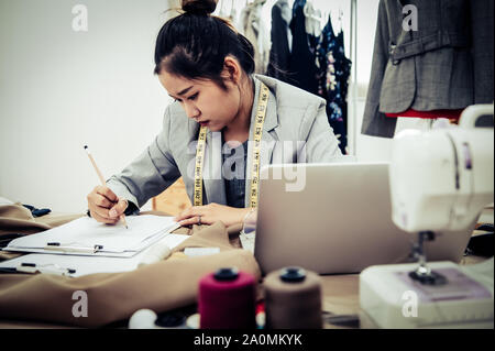 Business Asian fashion designer have no idea when designing new collection of dress in workshop studio. Dressmaker headache and negative thinking conc Stock Photo