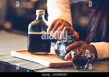 Closeup of professional female barista hand opening bottle of coffee to making cup of coffee. Happy young woman at counter bar in restaurant backgroun Stock Photo