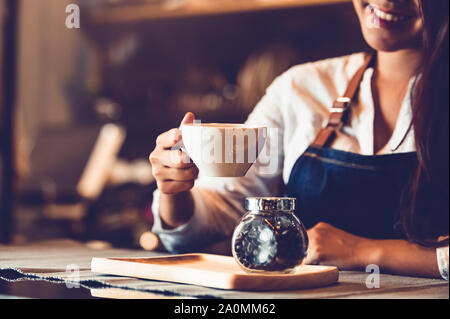 Closeup of professional female barista hand making and holding white cup of coffee. Happy young woman at counter bar in restaurant background. People Stock Photo