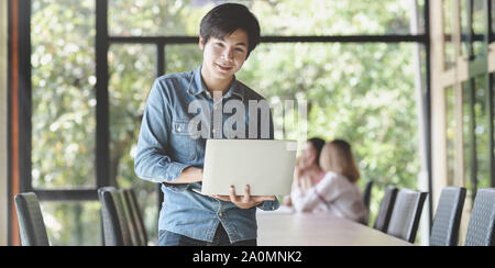Young male professional UX web developer standing in the meeting room and holding laptop computer Stock Photo