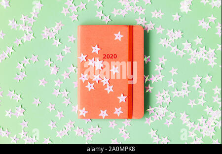 Orange diary for 2020 on a mint background strewn with light pink stars. Stock Photo