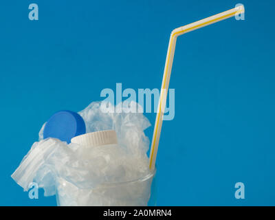 Glass with plastic inside on blue background with copy space - drinking plastic environmental concept Stock Photo