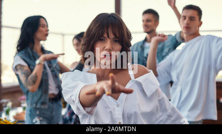 Dancing with friends. Pretty and young woman in white shirt is gesturing and looking at camera while standing on rooftop terrace with her friends. Party concept. Friendship Stock Photo