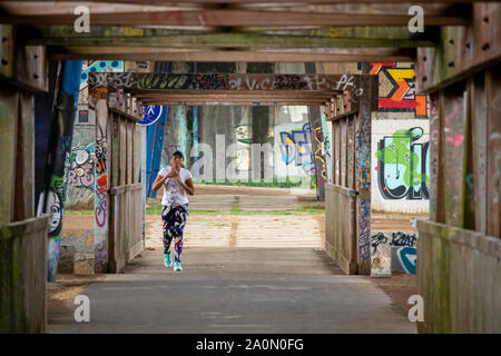 Coruna / Spain - September 20 2019: Lone woman walking across a wooden bridge covered in graffiti Stock Photo