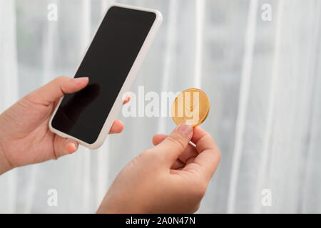 Holding crypto coin and mobile phone on white background Stock Photo