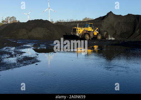 Germany, Hamburg, Hansaport import of hard coal and ore for steel plants and coal power stations, coal storage place in contrast with wind turbine of municipal electricity supplier Hamburg Energie Stock Photo