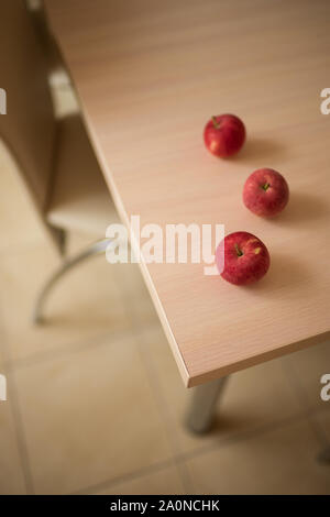 three red ripe apples on the wooden table in kitchen, room interior, top view, natural summer fruits. Stock Photo