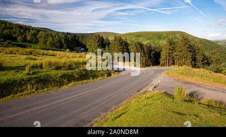 A narrow country lane winds across moorland and through plantation forest at Blaen-y-glyn high in the Brecon Beacons of South Wales. Stock Photo