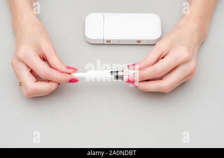 Woman's hands holds an electronic cigarette. Insert a cigarette into the  mouthpiece. Smoking, health, struggle, addiction Stock Photo