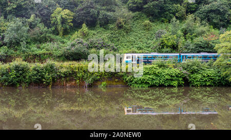 Cardiff, Wales, UK - July 19, 2019: A 2-car Pacer passenger train runs along the green banks of the River Taff at Radyr in the suburbs of Cardiff.