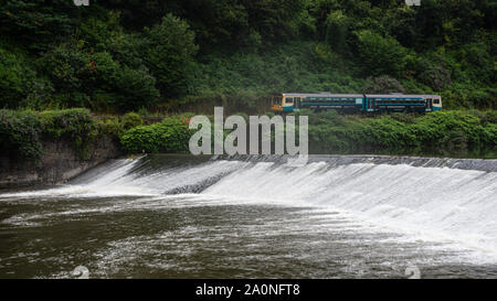 Cardiff, Wales, UK - July 19, 2019: A 2-car Pacer passenger train runs along the green banks of the River Taff at Radyr Weir in the suburbs of Cardiff