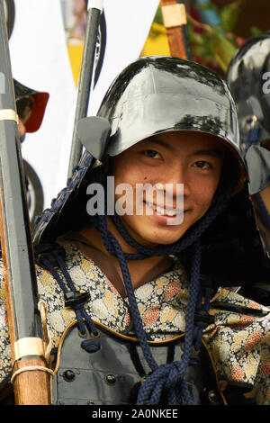 Smiling young Japanese reenactor dressed in traditional samurai costume and armour (armor) marches with rifle at samurai festival; Sarugakyo, Japan. Stock Photo