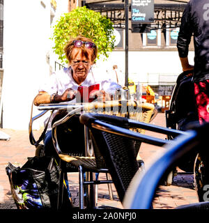Woman Sitting Alone Outside Using Her Mobile Phone Outside a Coffee Shop on a Sunny Day Stock Photo