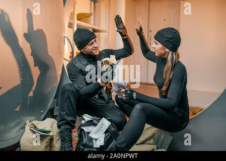 Two robbers in black uniform stuff bags with money Stock Photo