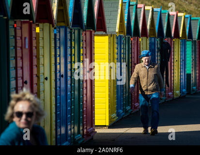 A man walks past brightly painted beach huts in Whitby, Yorkshire, as temperatures are expected to soar to 26C in some parts of the country this weekend. Stock Photo
