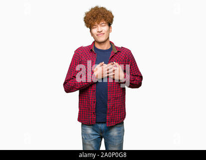Young handsome student man with afro hair wearing a jacket smiling with hands on chest with closed eyes and grateful gesture on face. Health concept. Stock Photo