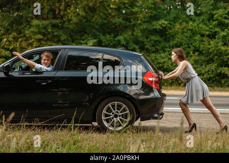 Young woman pushing broken car with man on road Stock Photo