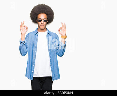 Young african american man with afro hair wearing thug life glasses relax and smiling with eyes closed doing meditation gesture with fingers. Yoga con Stock Photo