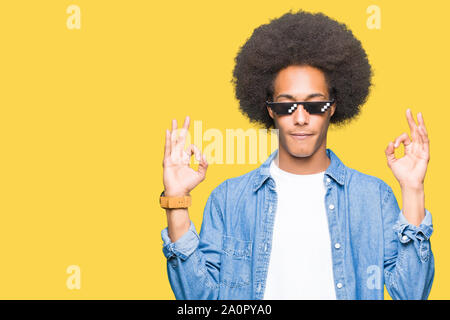 Young african american man with afro hair wearing thug life glasses relax and smiling with eyes closed doing meditation gesture with fingers. Yoga con Stock Photo