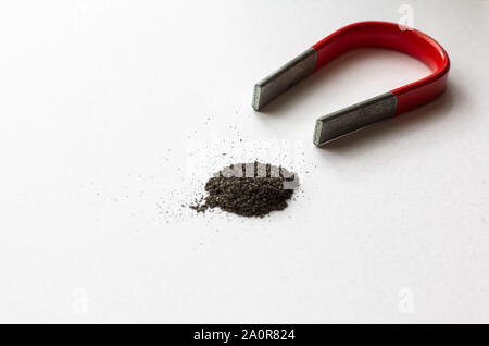 A horse shoe magnet next to a pile of iron filings on a white background Stock Photo