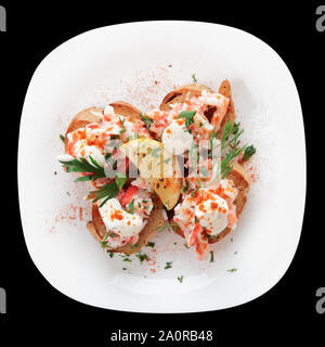 Crab meat with toast, sauce and fresh herbs in plate, isolated on black Stock Photo