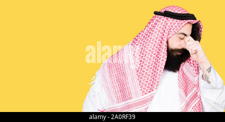 Arabian business man with long hair wearing traditional keffiyeh scarf tired rubbing nose and eyes feeling fatigue and headache. Stress and frustratio Stock Photo