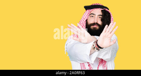 Arabian business man with long hair wearing traditional keffiyeh scarf Rejection expression crossing arms and palms doing negative sign, angry face Stock Photo