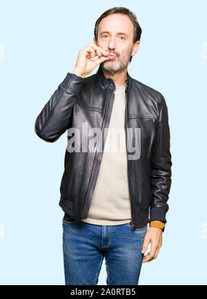 Middle age handsome man wearing black leather jacket mouth and lips shut as zip with fingers. Secret and silent, taboo talking Stock Photo