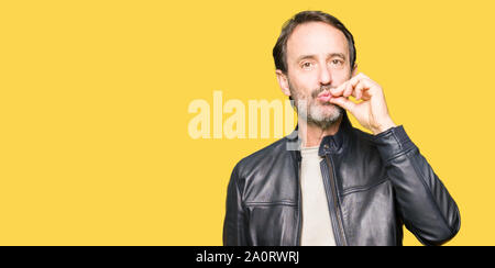 Middle age handsome man wearing black leather jacket mouth and lips shut as zip with fingers. Secret and silent, taboo talking Stock Photo
