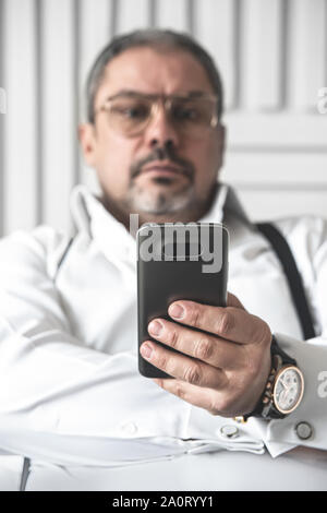 The bad news. A seriously displeased businessman in a white shirt is looking on the phone. foreground focus Stock Photo