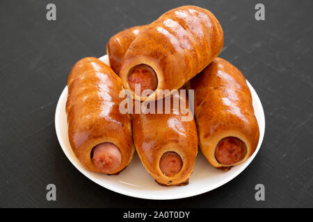 Homemade beef sausage kolache on a white plate on a black surface, side view. Close-up. Stock Photo