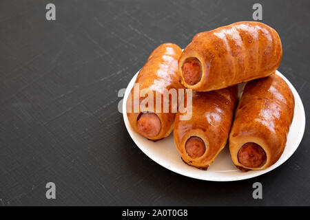 Homemade beef sausage kolache on a white plate on a black background, side view. Copy space. Stock Photo