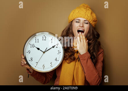 elegant woman in yellow beret and scarf with round clock yawning on bronze background. Stock Photo