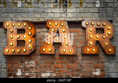 Bar signboard. Inscription from large metal letters decorated with glowing light bulbs on the brick wall Stock Photo