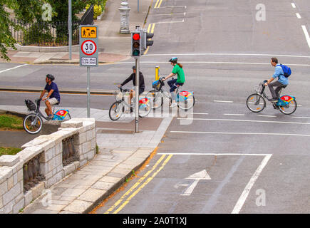 Four cyclists ride on hire bikes rental bicycles in dedicated cycle lane Dublin, Ireland. Environmentally friendly low carbon lifestyle Stock Photo
