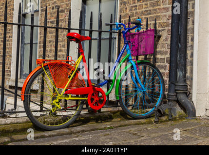 Colorful colourful bike bicycle in bold bright rainbow colors. At railings outside brick building. Red, orange, yellow, green, blue, indigo violet