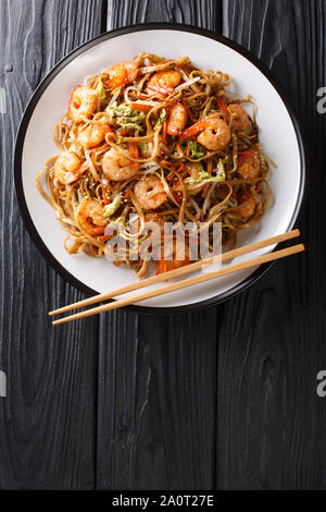 Tasty chow mein noodles with shrimp, vegetables and sesame seeds close-up on a plate on the table. Vertical top view from above Stock Photo